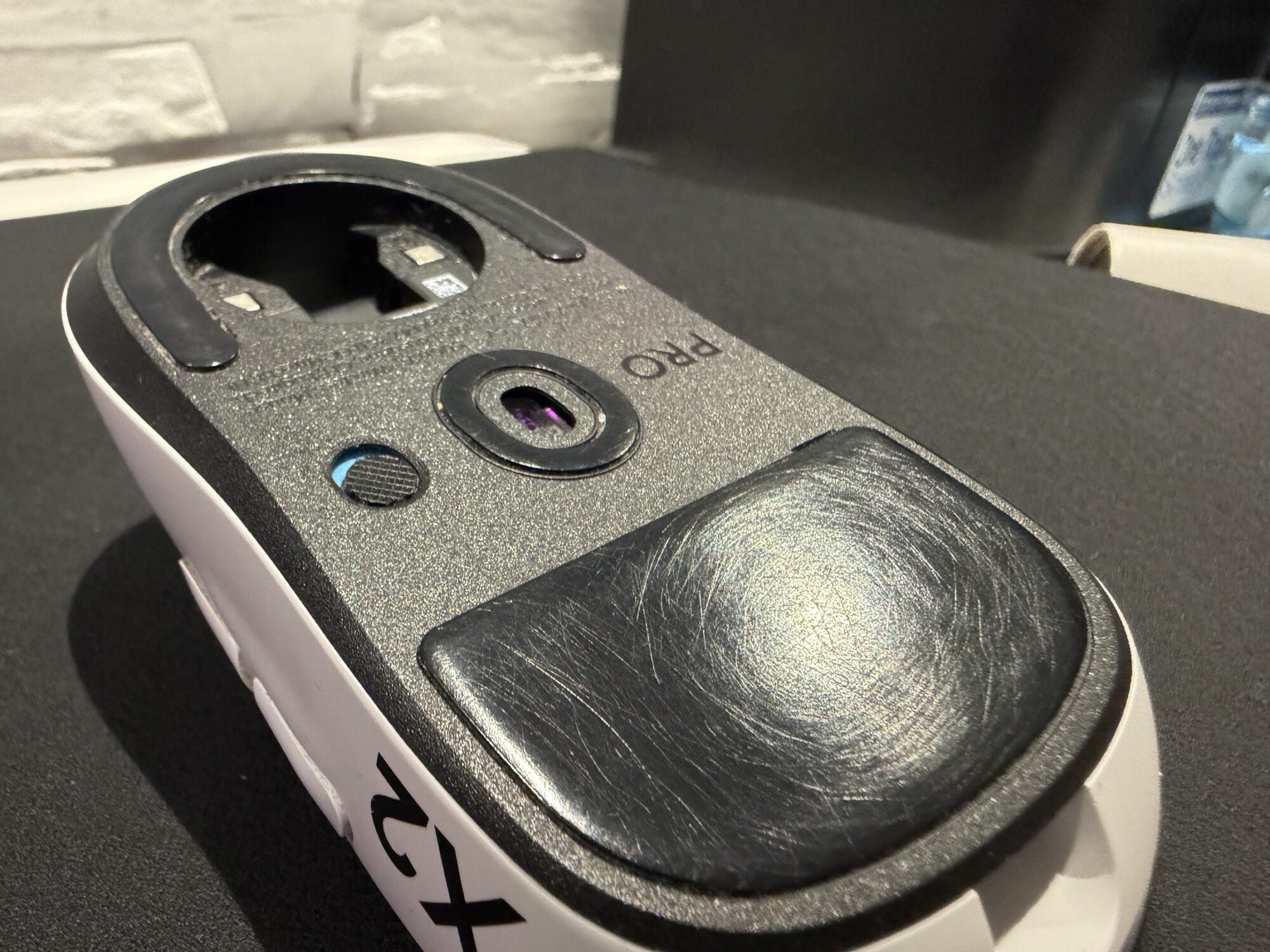 Jak czyścić podkładkę Artisan 2 Spód białej myszki Logitech z dużym czarnym ślizgaczem PTFE pokrytym gęstą siatką rys, z zachowaną zaokrągloną krawędzią